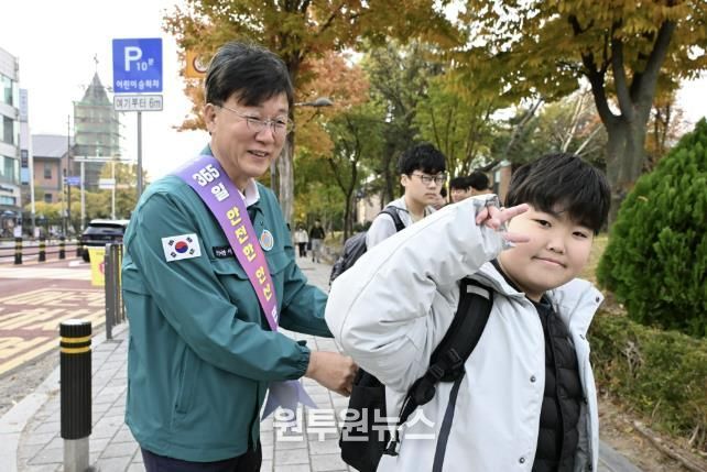 이민근 안산시장(사진 왼쪽)이 학현초등학교 앞에서 ‘스쿨존 어린이 교통안전 캠페인’을 진행하며 등교하는 어린이의 가방에 '홍이 키링'을 달아주고 있다.